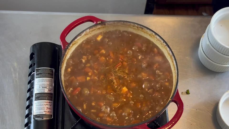 Steaming pot of gumbo with chicken, sausage, tomatoes, and vegetables in dark broth, moments before the lid goes on.
