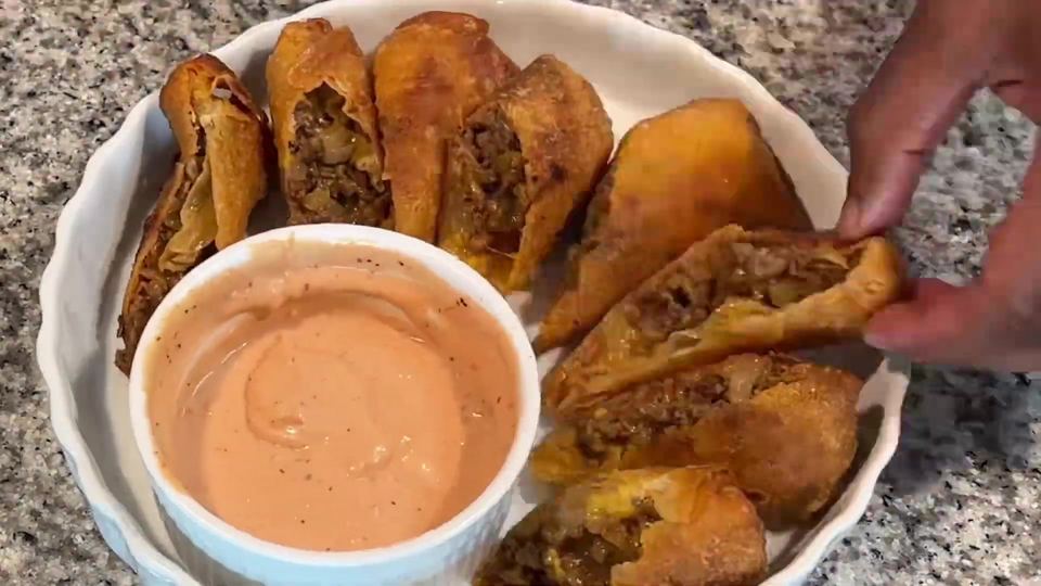 Halved chop cheese egg rolls showing the beef and cheese filling, plated around a ramekin of creamy dipping sauce.
