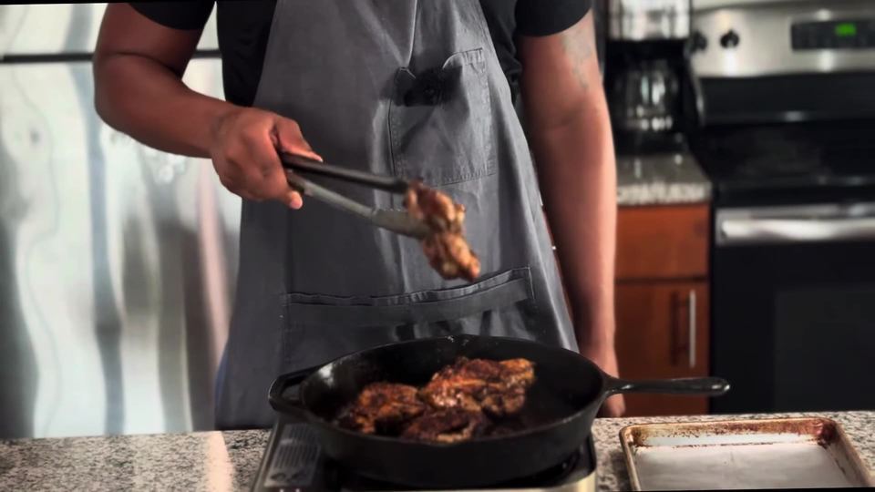 Deeply charred chicken thighs in a cast-iron skillet, one piece lifted with tongs mid-flip, with a sheet pan waiting alongside.