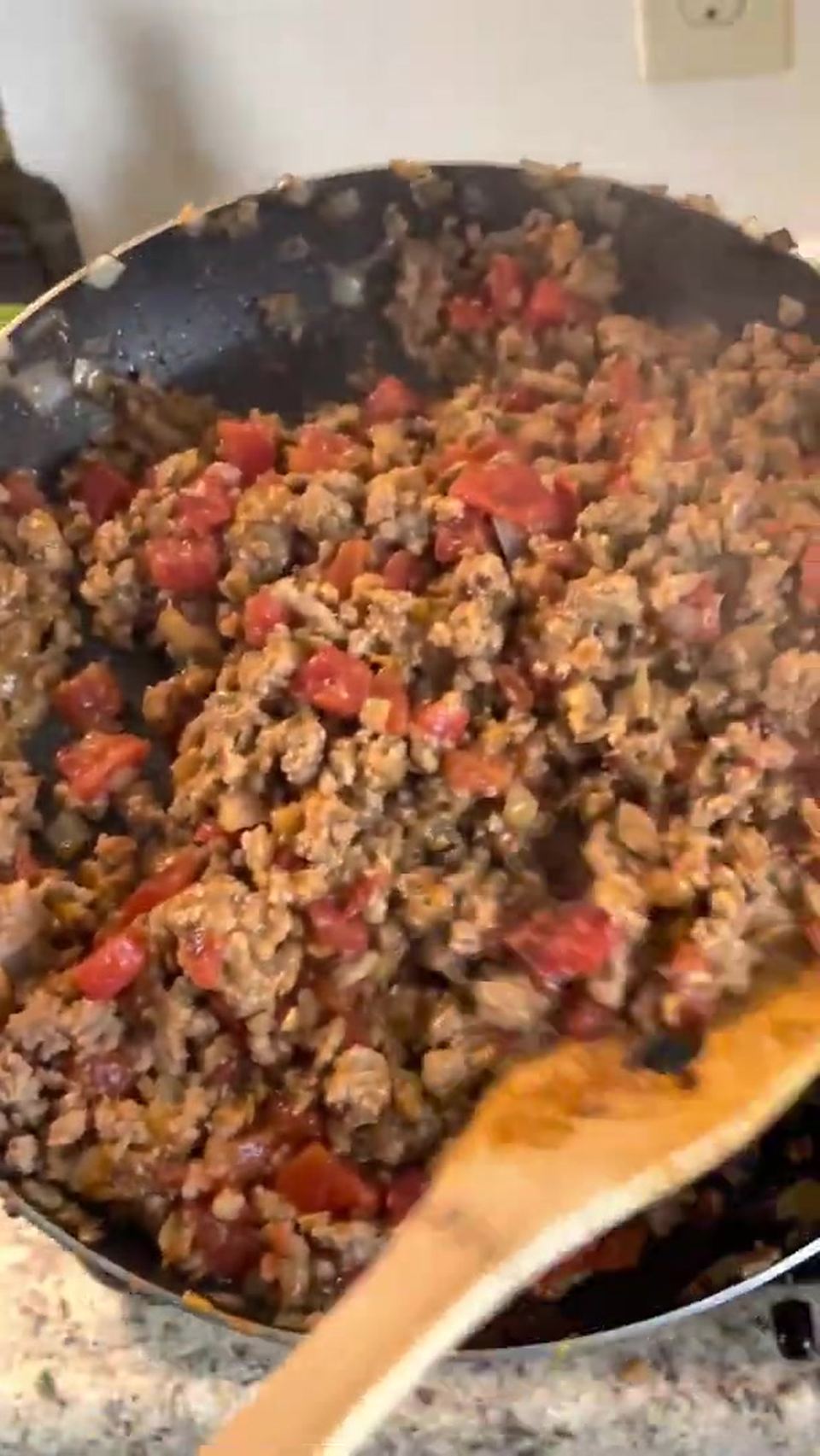 Thick taco meat of browned ground turkey, onions, and diced tomatoes with green chilies in a dark skillet, a wooden spoon at the pan's edge.
