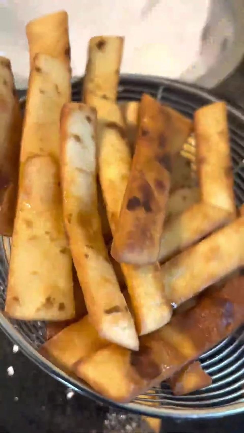 Golden-brown fried tortilla strips piled in a round wire spider strainer over the skillet.