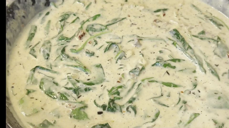 Thick, pale, creamy sauce in a cast-iron pan with wilted spinach leaves stirred throughout.