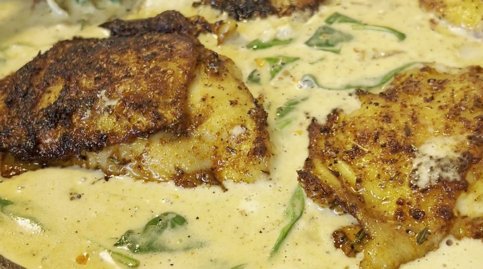 Seared chicken thighs with dark crusts nestled in a creamy sun-dried tomato and spinach sauce in a cast-iron skillet before baking.