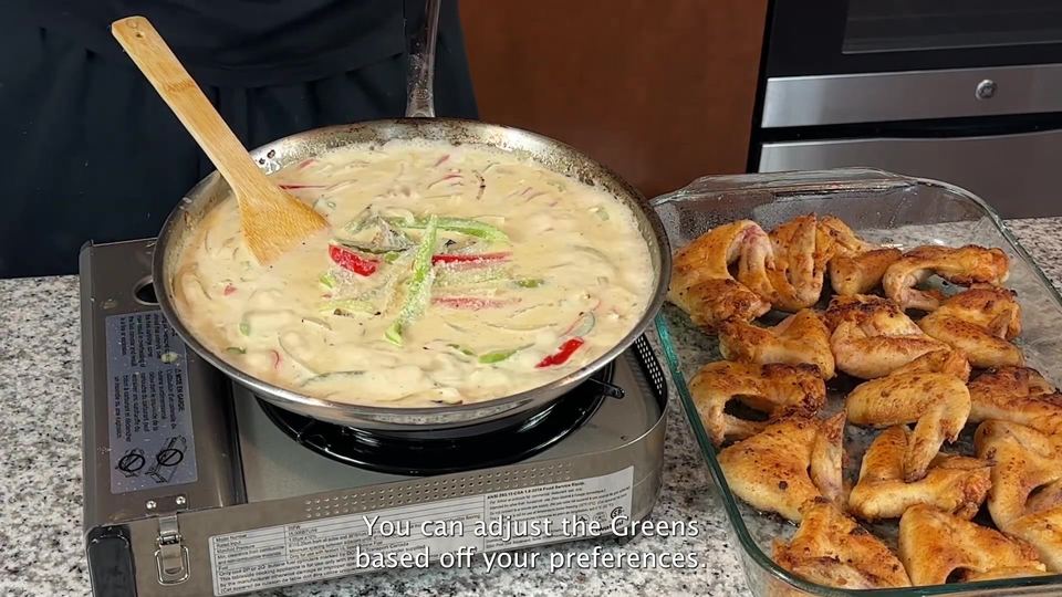 Wooden spatula resting in a skillet of pale creamy gravy with strips of red and green bell pepper and onion, next to a glass dish of fried wings.