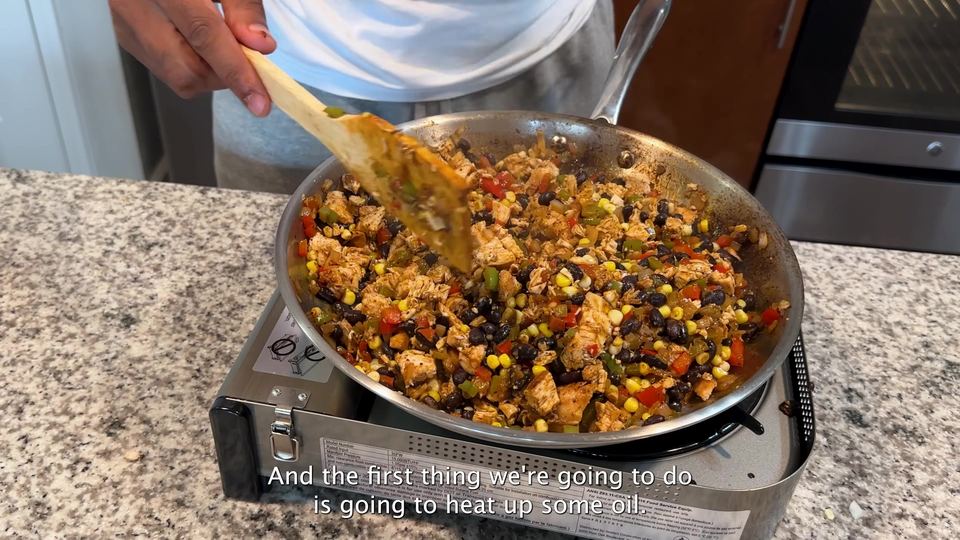 A stainless steel skillet of finished filling — diced chicken, black beans, corn, and red and green peppers — being stirred with a wooden spatula.