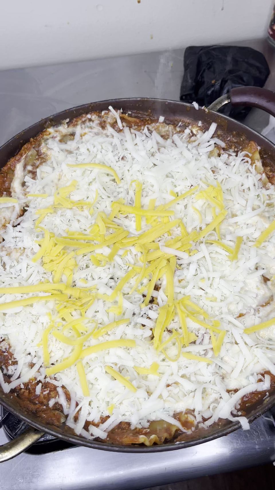 Skillet lasagna covered edge to edge with shredded white cheese and strands of yellow cheddar, before covering with the lid to melt.